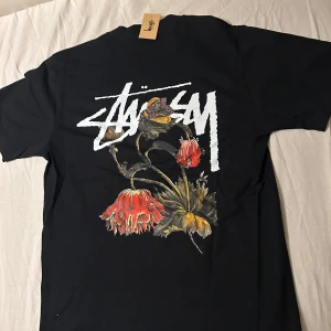 Stussy Svart T-shirt Stl. M Blommor - Absolut Helt Ny! (Med etikett dessutom)  Stussy T shirt storlek M.  Riktigt bra kvalitet, med hög kvalitet print bakom.  ~~Har andra modeller i sidan dessutom   Skriv vid frågor eller funderingar!!  Först till kvarn såklart! ;)