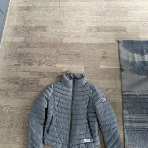 Grå dunjacka med dragkedja - Snygg grå dunjacka med dragkedja och hög krage. Perfekt för kyliga dagar. Jackan har en quiltad design och två praktiska fickor med dragkedjor.