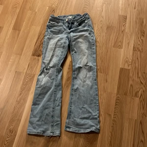 Blå jeans från Gina Tricot - Säljer ett par blå jeans från Gina Tricot i storlek 152. Byxorna har en bootcut-stil med slitna detaljer på knäna och en klassisk femficksdesign. Perfekta för en avslappnad look.