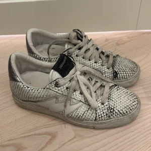 Vita sneakers med ormskinnsmönster från Zadig & Voltaire - Snygga vita sneakers med ormskinnsmönster från Zadig & Voltaire. Skorna har en unik design med silverdetaljer på hälen. Storlek 38 