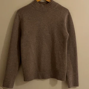 Beige stickad tröja - SANDÖ - Säljer en mysig beige stickad tröja med ribbad krage och muddar. Perfekt för kyliga dagar och ger en stilren look. 