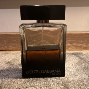 Dolce & Gabbana The One Pour Homme Eau de Parfum - Säljer en elegant herrparfym från Dolce & Gabbana, The One Pour Homme. Flaskan är stilrent designad i glas med en mörk toning och svart lock. Innehåller ungefär 50ml av en sofistikerad doft som passar perfekt för den moderna mannen.