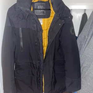 Svart vinterjacka från Decathlon storlek L - Säljer en svart jacka från Decathlon med gul quiltad insida. Jackan har en praktisk dragkedja och flera fickor framtill. Perfekt för kyligare dagar med sin långa ärm och skyddande huva.