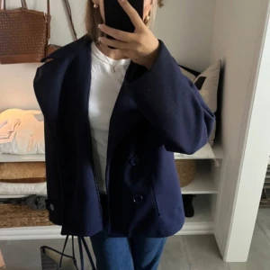 Mörkblå kappa med knappar - Snygg mörkblå kappa med stora knappar framtill. Jackan har en elegant krage och långa ärmar, perfekt för kyligare dagar. Den har en klassisk och stilren design som passar till många olika outfits.