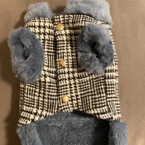 Rutig pälsjacka med knappar till hundar  - Säljer en stilren rutig jacka med mjukt pälsfoder i grått. Jackan har guldknappar framtill och är perfekt för kyliga dagar. Den har en klassisk look med ett modernt twist. Köpte fel storlek till min hund. Den är helt ny och den är i storlek S.  Den är lite grå blandat med mörk blå. Kontakta mig för fler frågor❤️