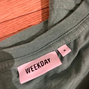 Grön t-shirt från Weekday - Säljer en stilren grön t-shirt från Weekday i storlek M. Perfekt för en avslappnad look. T-shirten har en klassisk rund halsringning och är kortärmad.