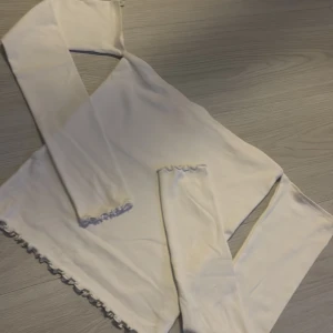 Vit långärmad topp med spetsdetaljer - Säljer en vit långärmad topp med fina spetsdetaljer vid ärmslut och nederkant. Perfekt för en stilren look.