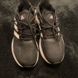 Svarta Adidas sneakers med vita detaljer - Säljer ett par svarta Adidas sneakers med vita ränder och snörning. Skorna har en sportig design med en bekväm sula, perfekt för vardagsbruk. Har använt dom 1 gång men dom va för små 
