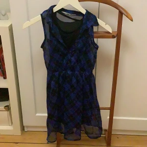 Blårutig ärmlös klänning från H&M - Blå och svart rutig klänning med knappar från HM perfekt till vardagar och speciella tillfällen. Klänningen har tillhörande svart underklänning. Klänningen har en reva i underklännings linningen men är inte synligt när man har på klänningen 