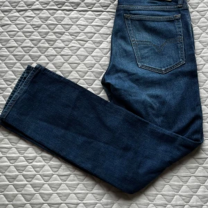 Blå jeans från Diesel - Snygga blå jeans från Diesel med klassisk design. De har en rak passform och är tillverkade i slitstarkt denim. Perfekta för en avslappnad stil. De är knappt använda och är i mycket gott skick, enda som är lite avvikande är att själva diesel patchen på något sätt har vikts lite i hörnet (syns på bild). Hör gärna av er vid frågor eller funderingar.