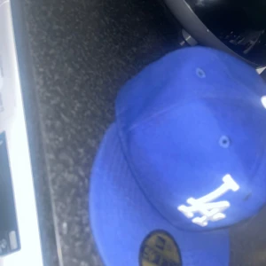 Blå keps med LA-logga - Snygg blå keps från New Era med LA-logga framtill. Kepsen har en klassisk 59FIFTY design och en platt skärm. Perfekt för att ge din outfit en sportig touch.