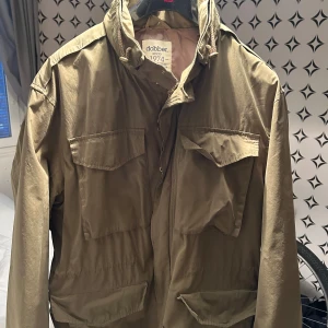 Olivgrön jacka från Dobber - Säljer en olivgrön jacka från Dobber med praktiska fickor och dragkedja. Perfekt för höst och vår. Jackan har en klassisk design med krage och knappar.