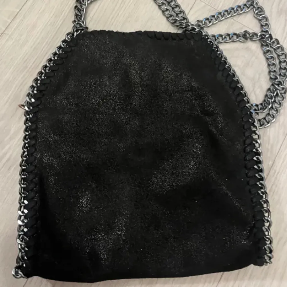 Snygg svart axelväska med glittrig yta och kedjedetaljer längs kanterna. Perfekt för att ge en edgy touch till din outfit. Väskan har en stilren design och är lätt att matcha med olika stilar.. Laukut & Käsilaukut.