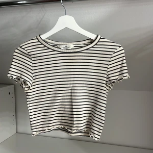 Randig ribbad topp från H&M - Säljer en randig ribbad topp från H&M i svart och vit. Toppen har korta ärmar  med vågiga kanter vid ärmslut och nederkant. Storlek 146/152