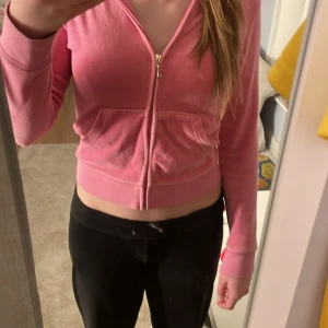 Rosa hoodie från Juicy Couture - Säljer en snygg rosa hoodie från Juicy Couture med dragkedja och huva. Den har ett dekorativt emblem på ryggen och en guldfärgad dragkedja med ett J-format handtag. Perfekt för en avslappnad stil. VIKTIGT‼️‼️Jag som har stl: xs, xxs passar den bra så som jag skulle vilja ha den men färgen är inte riktigt min så säljer den pågrund av det.