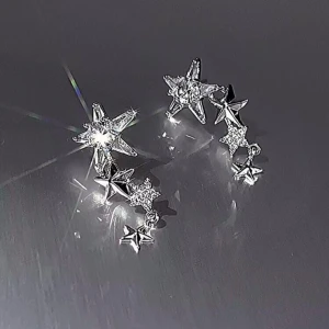 Silvriga stjärnformade örhängen - Eleganta silvriga örhängen med stjärnformade detaljer. De har en glittrig yta som fångar ljuset vackert och ger en stjärnklar känsla. Perfekta för att lägga till en gnistrande touch till din look.