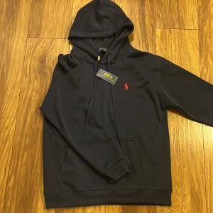 Mörk blå hoodie från Polo Ralph Lauren - Snygg stilig mörk blå hoodie från Polo Ralph Lauren. Perfekt för en avslappnad stil. Helt ny sitter som en M men står L i hoodien.