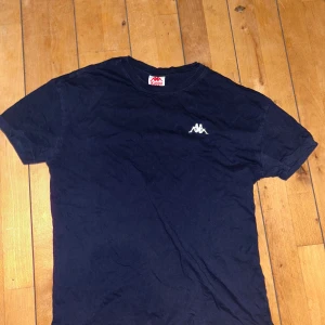 Svart t-shirt från Kappa - Säljer en klassisk svart t-shirt från Kappa med deras ikoniska logga broderad på bröstet. T-shirten är kortärmad och tillverkad i mjukt material för en bekväm passform. Perfekt för en avslappnad stil.