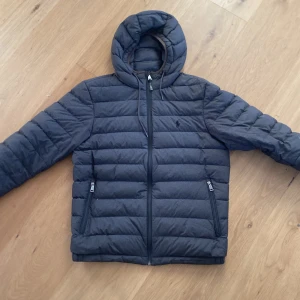 Grå dunjacka från Polo Ralph Lauren - Säljer en dunjacka från ralph lauren, jackan är grå och passar någon 175 perfekt. Jackan har skick 8/10 finns en liten färgklick på insidan men inget man ser vid användning ( bild 4)