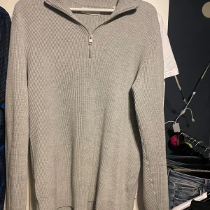 Grå ribbad tröja med dragkedja - Snygg grå ribbad tröja med dragkedja vid halsen. Perfekt för kyligare dagar med sin långärmade design. Enkel och stilren, passar till många olika outfits.