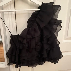 Svart off-shoulder topp från Gina  - Svart off-shoulder topp från Gina med volanger. Helt oanvänd, prislappen finns kvar. Storlek 36. Slutsåld på hemsidan 