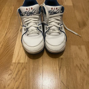 Vita Nike Air Flight sneakers - Snygga vita Nike Air Flight sneakers med blå och röda detaljer. Skorna har klassisk snörning och en bekväm passform. Perfekta för en sportig look. Storlek:41 i otroligt bra skick. Nypris 1200