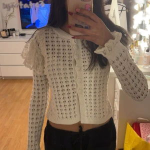 Vit stickad kofta från Zara - Säljer en söt vit stickad kofta från Zara med volangdetaljer på axlarna. Koftan har långa ärmar och knappar framtill. 