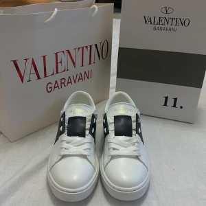 Valentino Garavani sneakers - Snygga vita Valentino Garavani sneakers med svarta detaljer och snörning. Perfekta för en stilren look med en touch av lyx.