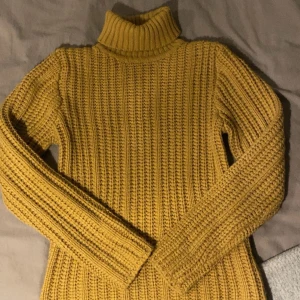 Gul stickad polotröja - Säljer en mysig gul stickad polotröja med ribbad design. Perfekt för kyliga dagar med sin höga krage och långa ärmar. Ett måste för garderoben!