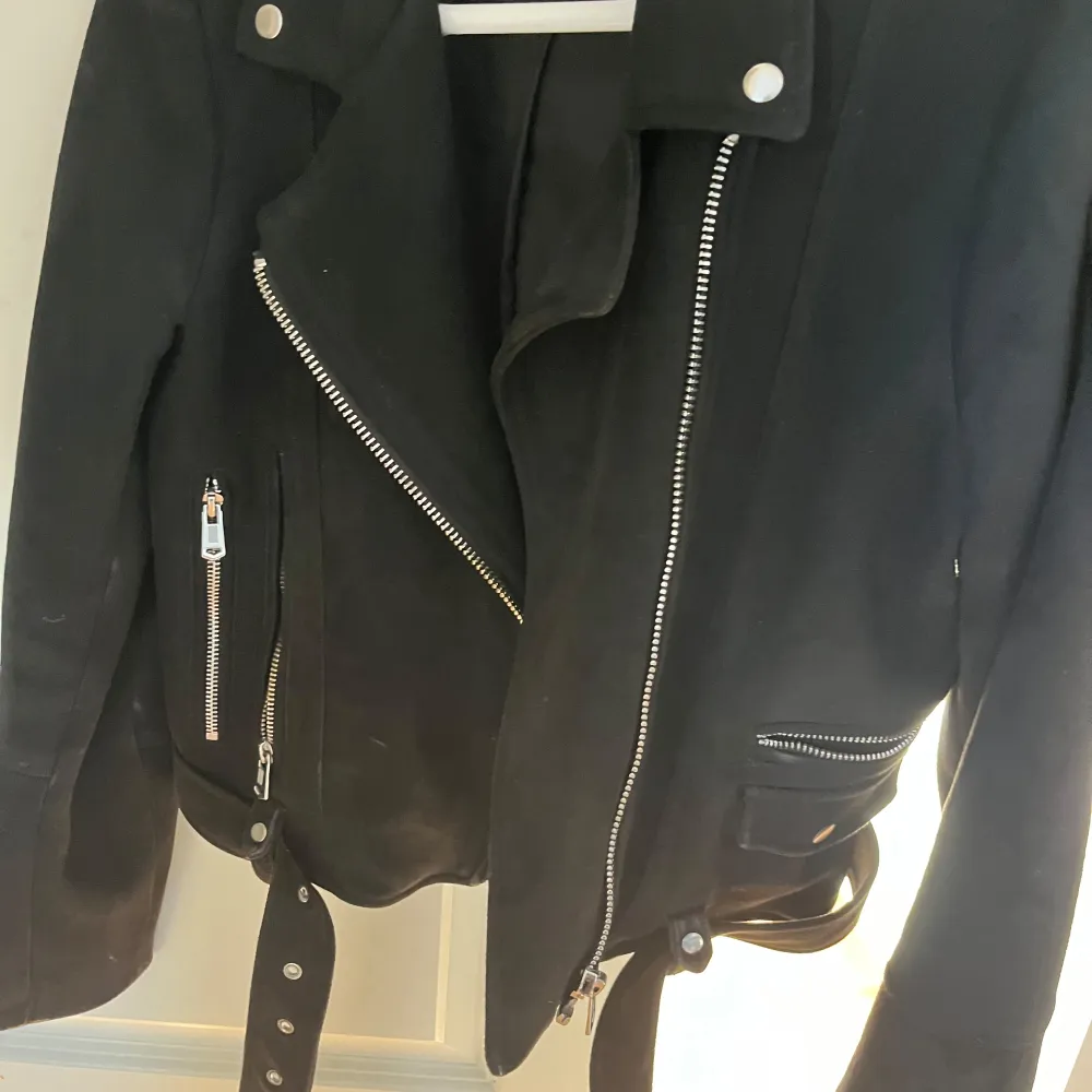 Snygg svart skinnjacka från Zara med dragkedjor och bälte i midjan. Jackan har långa ärmar och axelklaffar med knappar. Perfekt för en cool look.. Takit.