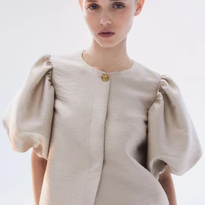 Beige topp med puffärmar - Säljer en superfin beige topp med puffärmar och en elegant guldknapp framtill. Perfekt för både vardag och fest! 💫