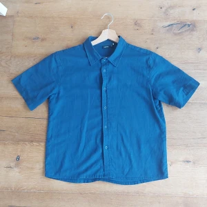 Blå kortärmad skjorta från LMTD - Säljer en snygg blå kortärmad skjorta från LMTD i storlek XS (146- 152cm). Perfekt för sommardagar eller avslappnade tillfällen. Skjortan har en klassisk krage och knappar framtill. Den är i bra skick och redo för nya äventyr! använd fåtal gånger! Pris kan diskuteras