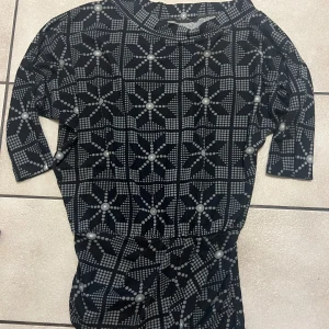 Svart och grå mönstrad vinter klänning - Snygg svart klänning med geometriskt mönster i grått. Klänningen har trekvartsärmar och en bekväm passform. Perfekt för en stilren look. Klänningen är one size.