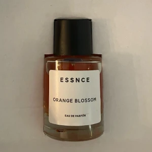 ESSNCE Orange Blossom Eau de Parfum - Upptäck ESSNCE Orange Blossom, en elegant Eau de Parfum med en fräsch och blommig doft av apelsinblomma. Flaskan är stilren och genomskinlig med en svart kork, vilket ger en modern och minimalistisk känsla.