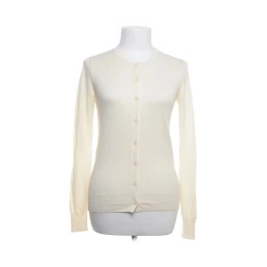 Kofta - Säljer en stilren beige/gul kofta från Uniqlo. Koftan har långa ärmar och knappar framtill, perfekt för alla årstider.