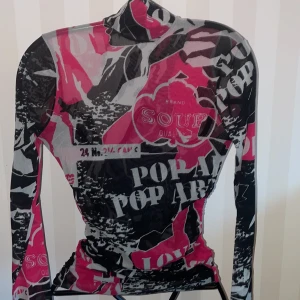 Pop Art mönstrad tröja från United Colors of Benetton - Snygg och unik tröja med pop art-mönster i svart, grått och rosa från United Colors of Benetton. Tröjan har en tight passform och långa ärmar, perfekt för att sticka ut i mängden.