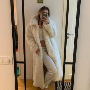 Vit lång teddyjacka - Säljer en supermysig vit teddyjacka som är lång och perfekt för kyliga dagar. Jackan har en fluffig textur och långa ärmar, vilket gör den både stilren och bekväm. Perfekt för att hålla värmen med stil! HELT OANVÄND!