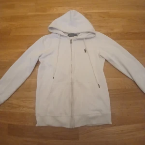 Vit hoodie från Polo Ralph Lauren - Säljer en stilren vit hoodie från Polo Ralph Lauren med dragkedja och den klassiska loggan på bröstet. Perfekt för en avslappnad look. Den har en justerbar huva och långa ärmar. Bra Fin pris. Pris kan diskuteras.