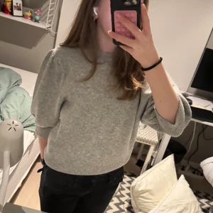 Grå stickad tröja - Säljer en mysig grå stickad tröja med trekvartsärm. Perfekt för kyliga dagar och enkel att matcha med olika outfits.