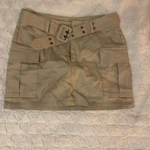 Beige kjol med bälte - Snygg beige kortkjol med ett matchande bälte och stora fickor framtill. Som ny:)