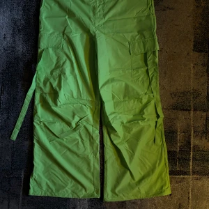 Gröna cargopants med vida ben - Snygga gröna cargopants med vida ben och praktiska fickor på sidorna. Byxorna har en avslappnad passform och knytdetalj i midjan för justerbarhet. Perfekta för en cool och avslappnad stil.