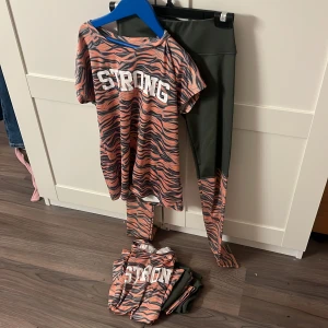 Två träning sett OTP Young - Säljer två träningsett från OTP Young med texten 'STRONG' på framsidan. Toppen har ett orange och grått zebramönster och korta ärmar. Om du bara vill ha ett sett kostar det 50 för båda blir det 80. En av dom har ett litet hål i byxan