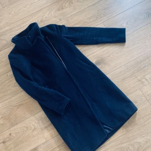 Mörkblå kappa från Tiger of Sweden - Elegant mörkblå kappa från Tiger of Sweden. Den har en stilren design med långa ärmar och en hög krage. Perfekt för kyligare dagar och ger en sofistikerad look.