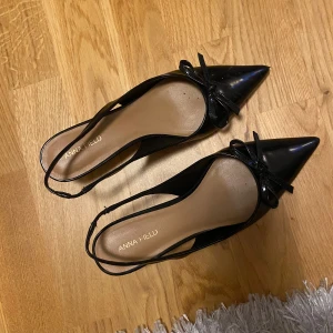 Svarta klackskor med rosett - Svarta glansiga klackskor med spetsig tå. Använda en gång. Kommer med sin låda