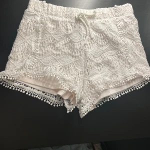 Vita spets shorts från Jessica Simpson - Snygga vita shorts i spets från Jessica Simpson. De har en elastisk midja med knytband och fina spetsdetaljer längs kanterna. Perfekta för en somrig look!🫶🏼