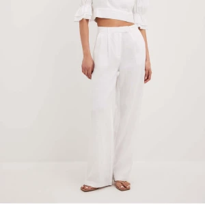 Vita linnebyxor med hög midja - Helt oanvända snygga vita linnebyxor med hög midja och vida ben från NA-KD. Perfekta för en stilren look. Byxorna har en knäppning fram och är tillverkade i ett luftigt material som passar bra för varmare väder. Nypris 749kr. 