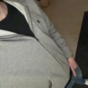 Grå hoodie från Polo Ralph Lauren - Säljer en stilren grå hoodie från Polo Ralph Lauren med dragkedja och det klassiska logotypbroderiet på bröstet. Perfekt för en avslappnad look. Hoodien har en mjuk insida och är tillverkad i bomull. Köpt på kidsbrandstore för 1100kr fast säljer nu för bara 600kr. Mycket bra kvalitet 