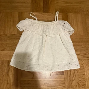 Vit axelbandslös topp från Lindex Kids - Söt vit axelbandslös topp från Lindex Kids med volangdetaljer och prickigt mönster. Perfekt för varma sommardagar.