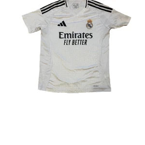 Real Madrid fotbollströja - Säljer en vit Real Madrid fotbollströja från Adidas med korta ärmar. Tröjan har klubbens emblem på bröstet och sponsorlogga 'Emirates Fly Better'. På baksidan finns namnet 'Mbappé' och nummer 9. Perfekt för inför säsongen!