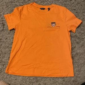 Orange t-shirt från GANT - Snygg orange t-shirt från GANT med ett tryck på bröstet. Perfekt för en avslappnad stil. Gjord i mjukt bomullsmaterial för extra komfort.